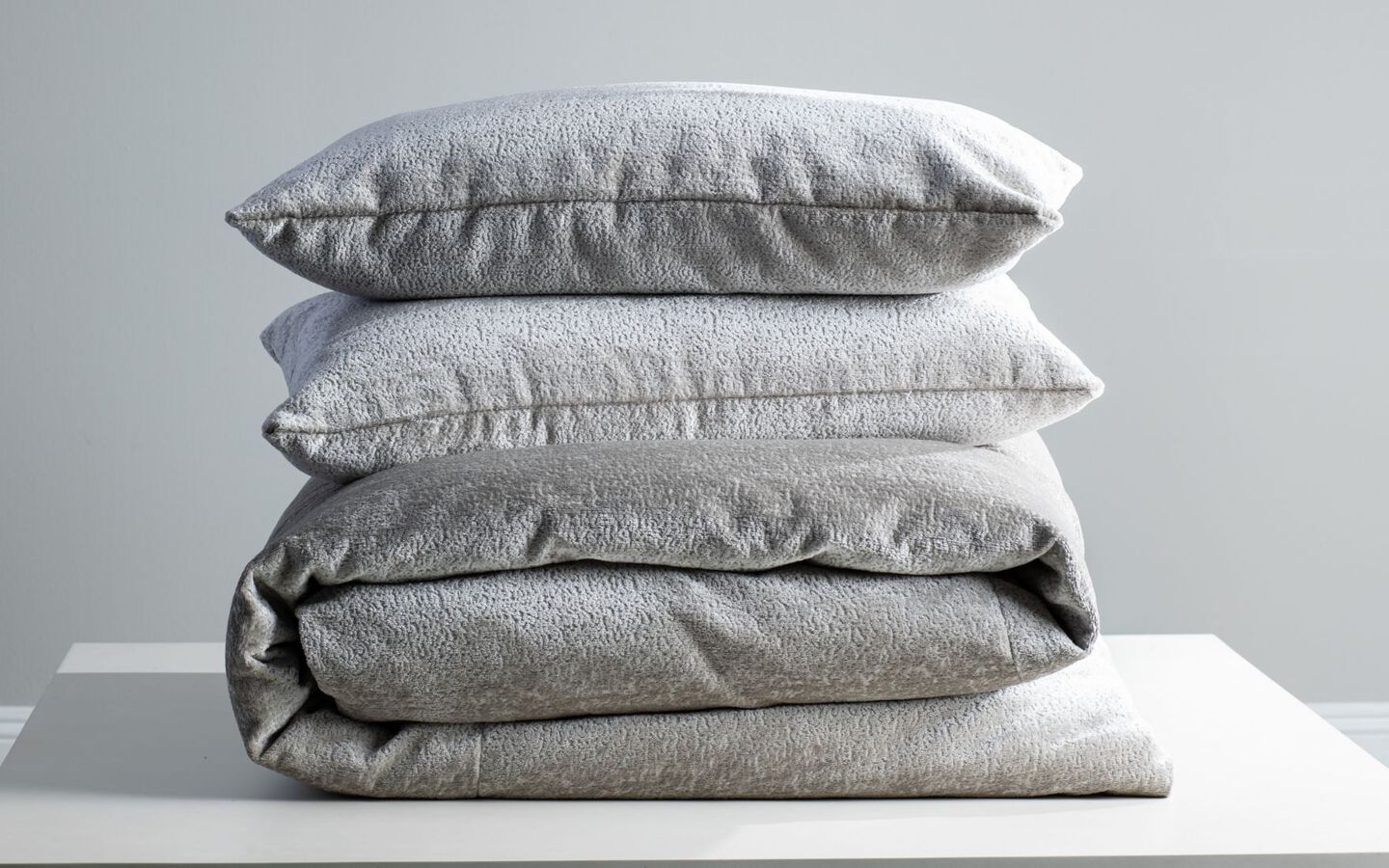 Closeup image of grey comforter and pillows stacked vertically