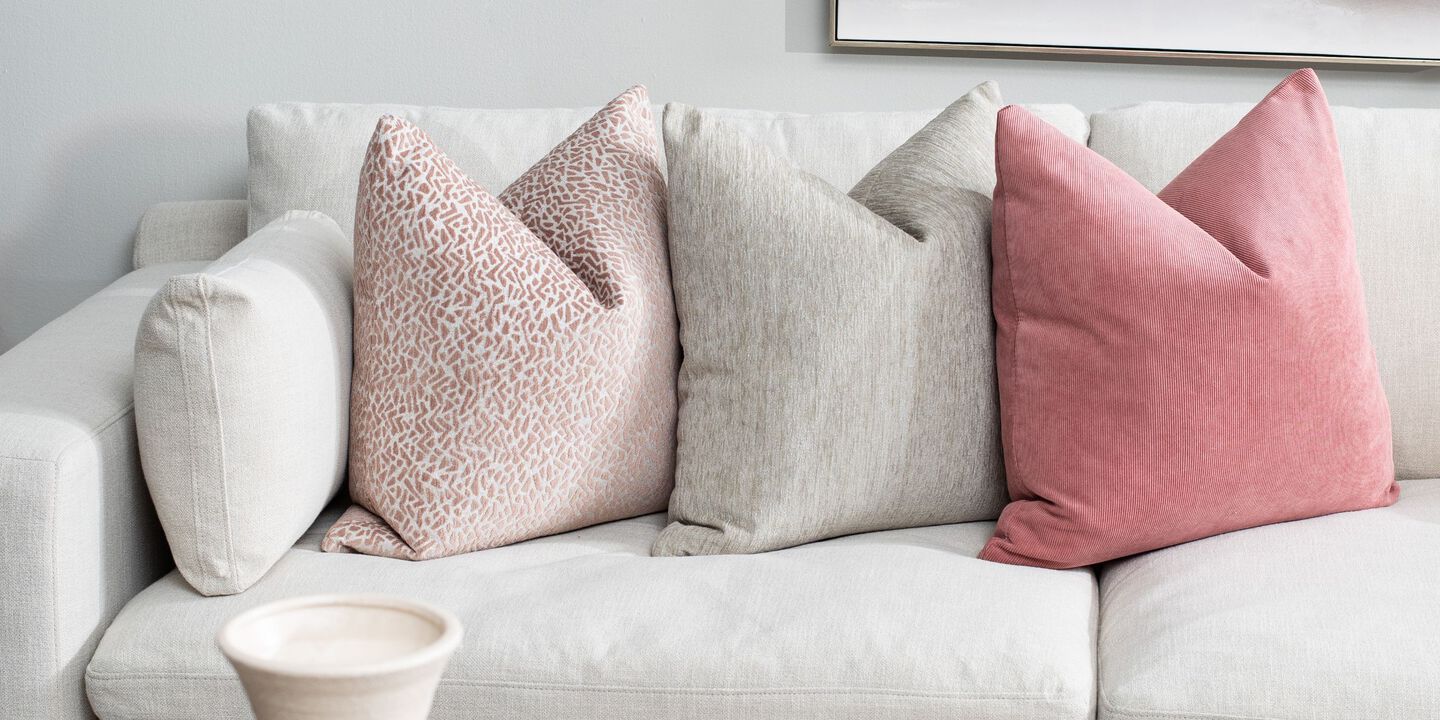 Light grey couch with throw pillows on top, one light gray and two pink