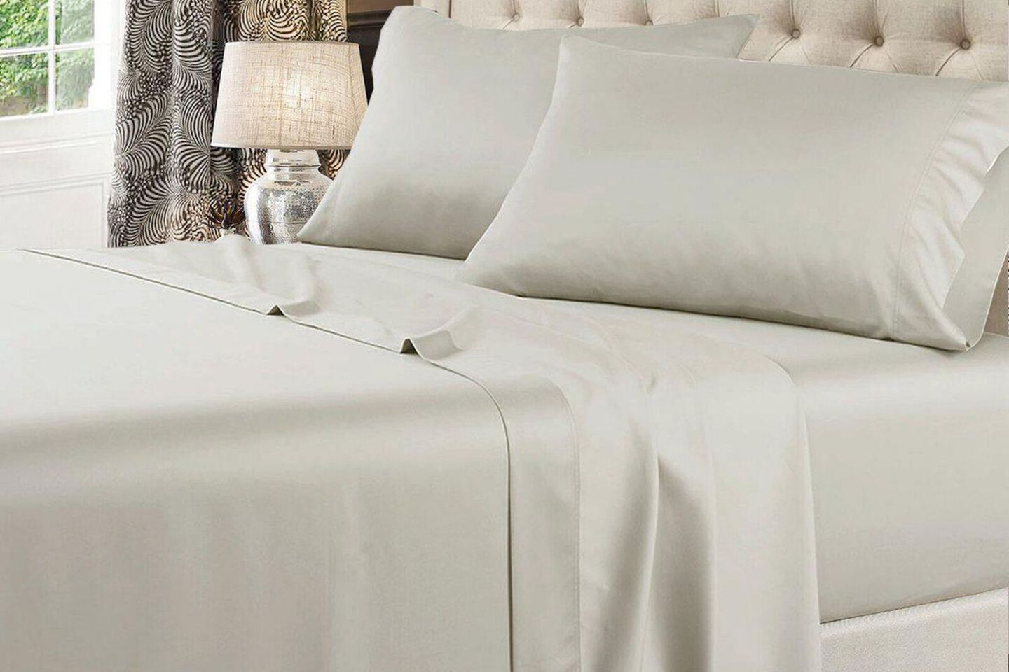 Tightly made bed with light grey sheets and pillows