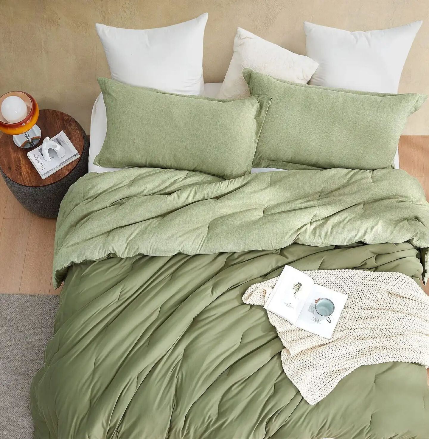 Bed with a light green bed spread, matching pillows, and a side table next to it