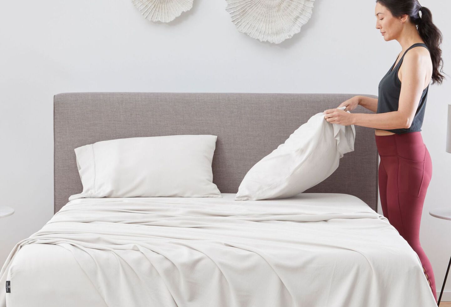 Woman putting a pillow in a pillowcase onto a bed with white sheets