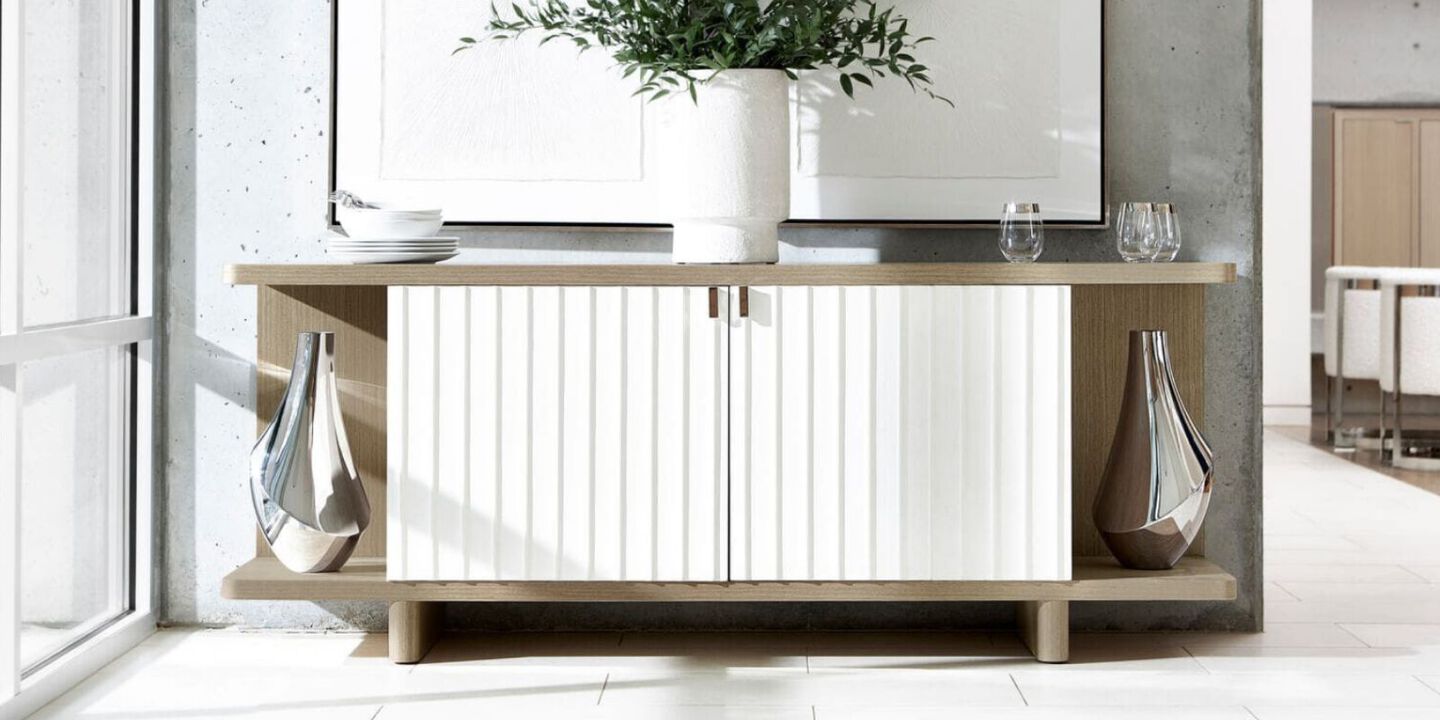 light wood sideboard with white paneling holding two silver vases and a fake plant 