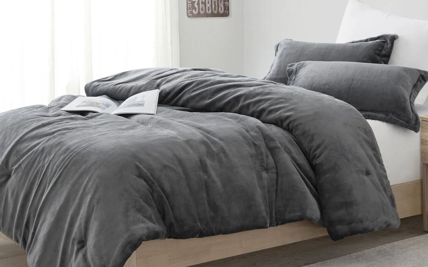 Bed with light wooden bedframe and dark grey comforter with matching pillows