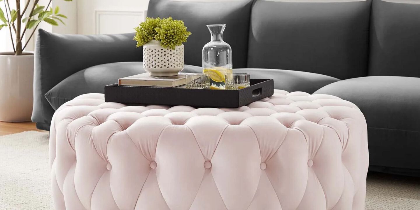 Pink plush ottoman with black tray on top in front of dark grey couch