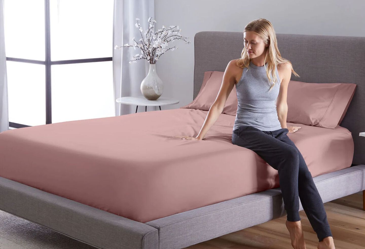 Woman sitting on top of a bed made with pink sheets and pillows