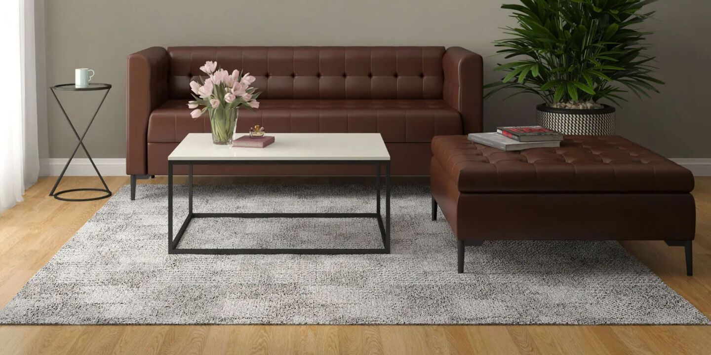 Living room with brown couch and matching ottoman, grey rug, and white and black coffee table