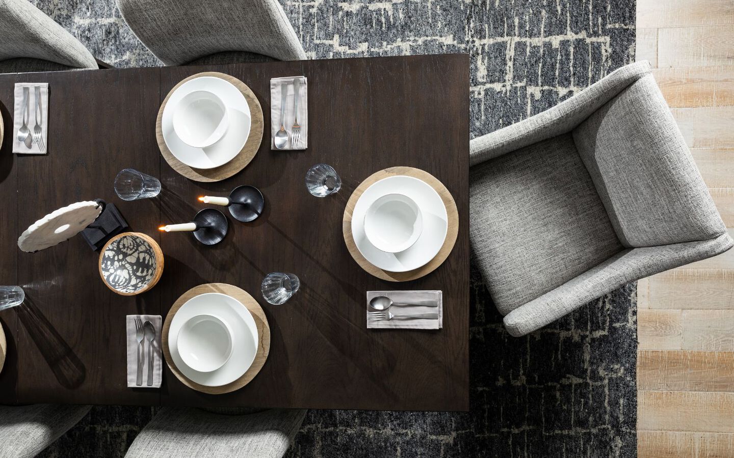 Aerial view of a dark brown dining table set with plates and cups surrounded by grey upholstered chairs