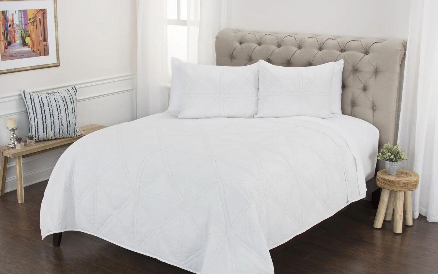 Bed made with white comforter and matching pillows sitting on top of a beige upholstered bedframe