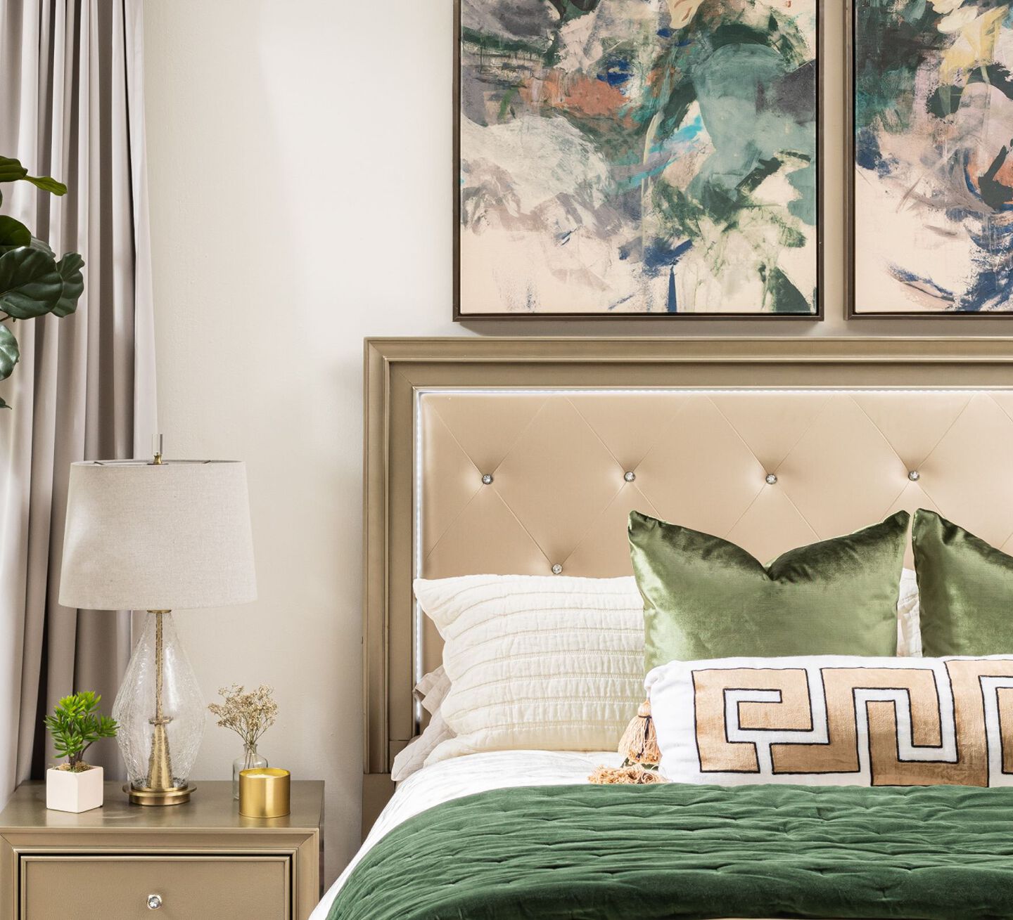 Bedroom with beige bed with green and white bedding sitting under two abstract paintings hanging on the wall