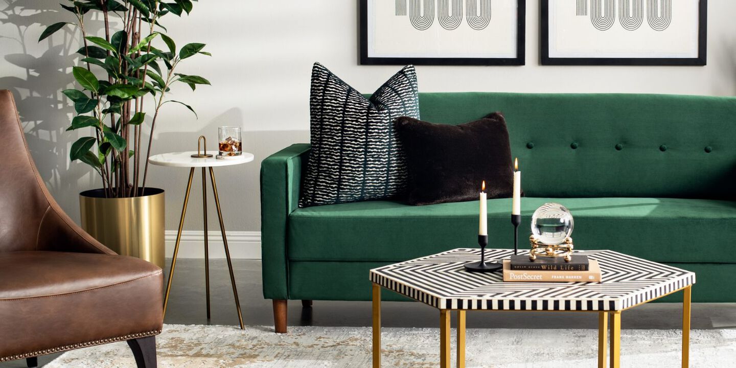 living room setting with green velvet couch with black pillows, a brown leather chair, and a black, white, and gold coffee table