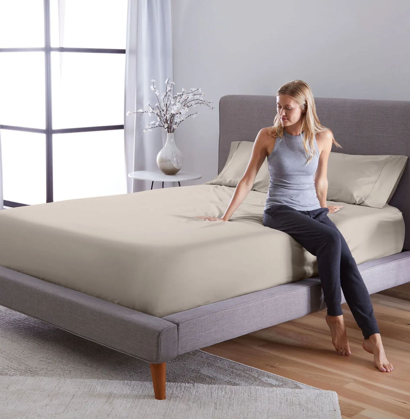 Woman sitting on the edge of a bed made with beige sheets