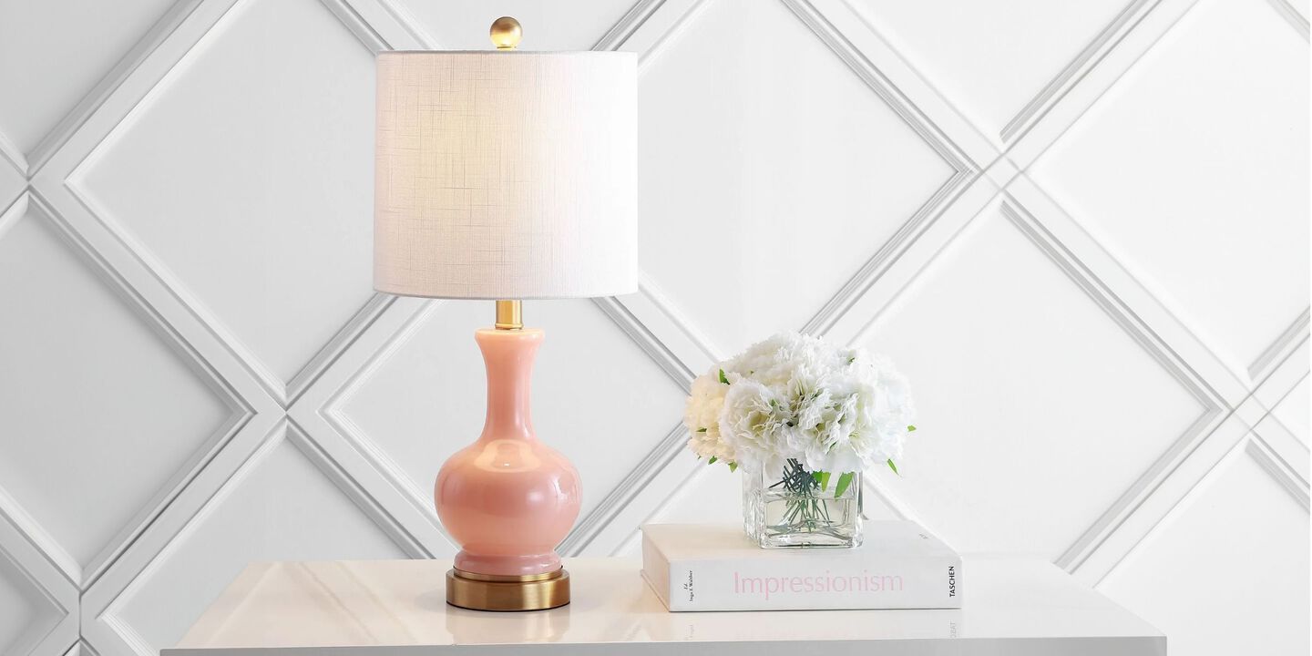 White table against a white wall with a pink lamp, white book, and vase of flowers on top