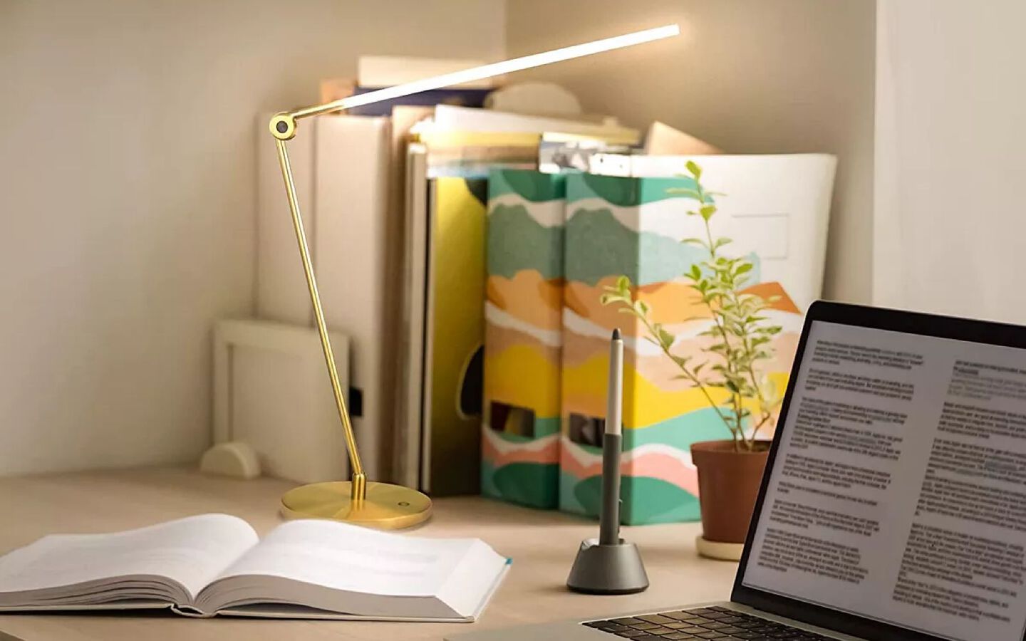 Desk with small gold lamp, binders, an open book, and a laptop