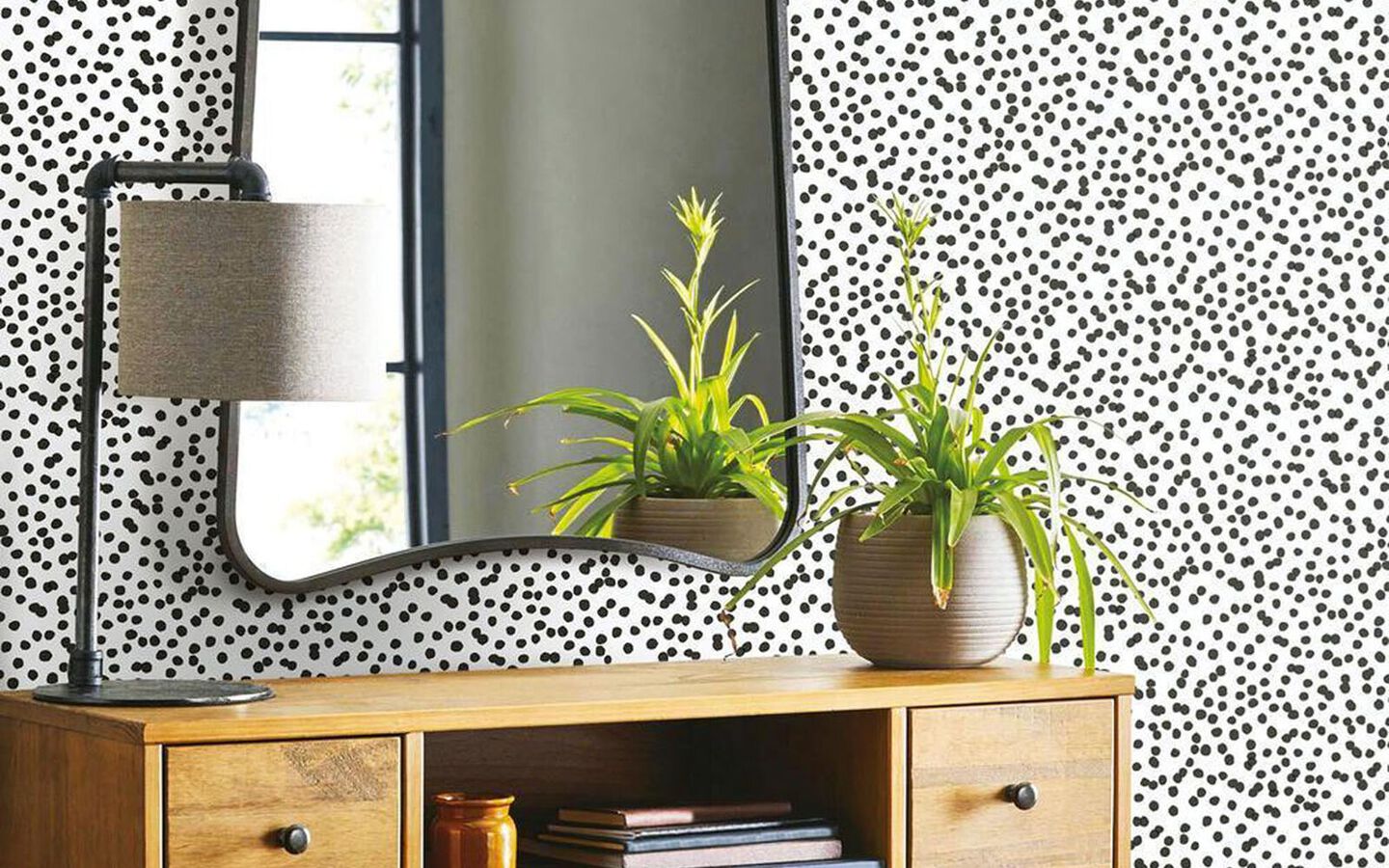 Dresser with lamp and plant sitting in front of a polka dot printed wall with hanging mirror