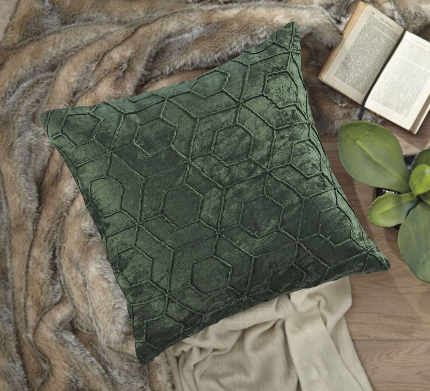 Green textured pillow on top of a brown blanket next to a plant and book