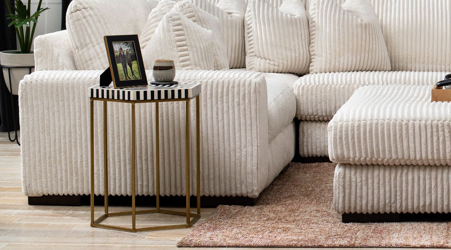 Living room with white sectional and ottoman next to a gold, black, and white side table